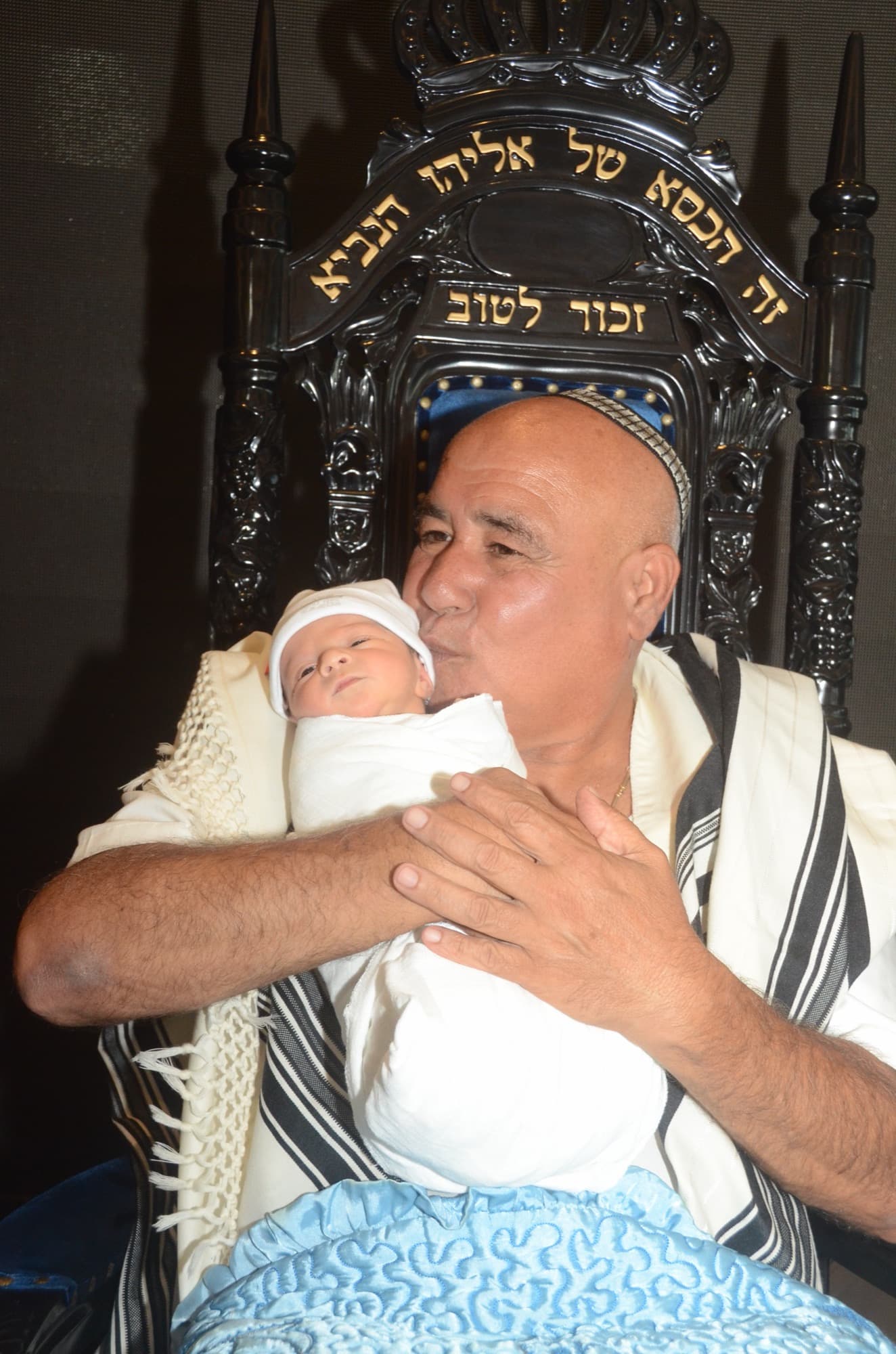 הסנדק מחזיק את התינוק על כיסא אליהו